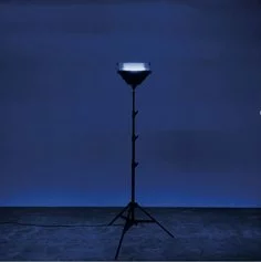 L’heure Bleue (2022) di Nina Carini. Time 2. Installazione luminosa e sonora con timer interno. Faro alogeno modificato, diffusore audio, vetro forato, amplificatore con player integrato, stativo, modulo programmabile con timer, disk usb